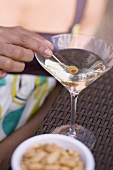 Woman holding green olive on cocktail stick in Martini glass