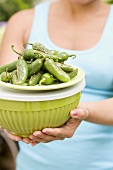 Woman holding grilled chillies on top of a green bowl