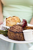Woman holding a plate of grilled steak and accompaniments