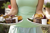 Woman serving two plates of grilled steak & accompaniments