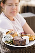 Grilled beef steak with accompaniments, woman in background