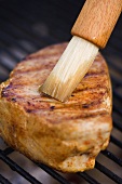 Steak on a barbecue being brushed with oil
