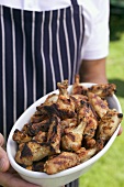 Man in apron holding grilled chicken wings