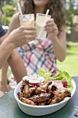 Grilled chicken wings with salad, young people in background