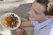 Young man holding plate of grilled steak & accompaniments