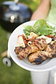 Woman holding plate of grilled chicken legs & pasta salad