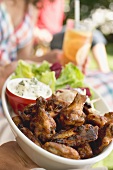 Hands holding chicken wings with salad, people in background
