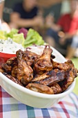 Person holding grilled chicken wings, people in background