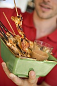 Man serving grilled satay with dip