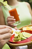 Hand holding basket of guacamole & chips, woman with tomato drink