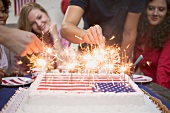 Hands lighting sparklers on a cake (4th of July, USA)
