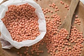 Red lentils on wooden plate and in bag (close-up)