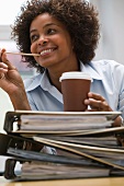Frau im Büro mit Kaffeebecher auf einem Stapel Akten