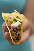 Hand holding taco filled with mince, cheese & sour cream