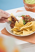 Hand dipping tortilla chip in mince sauce
