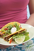 Woman holding plate with two tacos