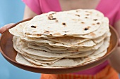 Frau hält frisch gebackene Tortillas auf Tablett