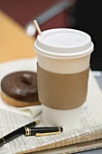Kaffee im Pappbecher und Doughnut auf Zeitung im Büro