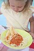 Small girl eating spaghetti with tomato sauce