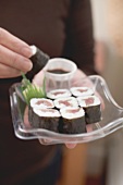 Woman holding maki sushi and soy sauce on plastic tray