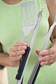 Woman holding barbecue tongs and spatula