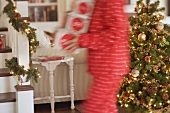 Frau trägt Schachteln mit Weihnachtsschmuck durch Wohnzimmer