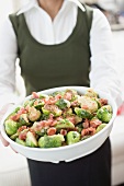 Woman holding Brussels sprouts with bacon in white dish