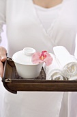 Woman holding towels, bowl and orchid on tray