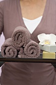 Woman holding towels, soaps and orchid on tray