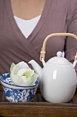 Frau hält Tablett mit Teekanne, Teeschale und Blüte
