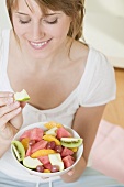 Woman eating wedge of apple from fruit salad