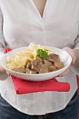 Woman holding plate of Zürcher Geschnetzeltes (veal dish) with pasta