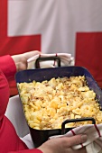 Woman serving cheese and onion pasta bake (Switzerland)