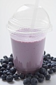Blueberry shake in plastic cup, surrounded by blueberries