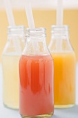 Three fruit juices in bottles with straws