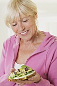 Woman holding slice of bread topped with sprouted seeds