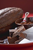 Pieces of chocolate in front of cocoa powder & cacao fruit