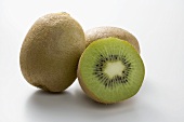 Half a kiwi fruit in front of two whole kiwi fruits