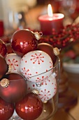 Assorted Christmas tree baubles in front of red candle