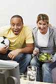 Paar mit Fussball und Salat vor dem Fernseher
