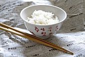 Rice in Asian bowl on newspaper, chopsticks beside it