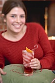 Woman holding glass of Campari with ice cubes in front of fireplace