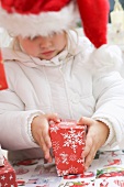 Kleines Mädchen mit Nikolausmütze öffnet Weihnachtspaket