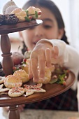 Girl reaching for Christmas biscuit on tiered stand