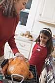 Young woman holding turkey in roasting dish, girl in background