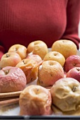Woman holding baked apples on baking tray (detail)