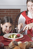 Young woman cutting up vegetables on small girl's plate