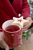 Woman holding mug of tea with jam biscuit