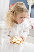 Small girl with angel's wings holding plate of biscuits