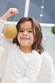 Kleines Mädchen hält goldene Christbaumkugel